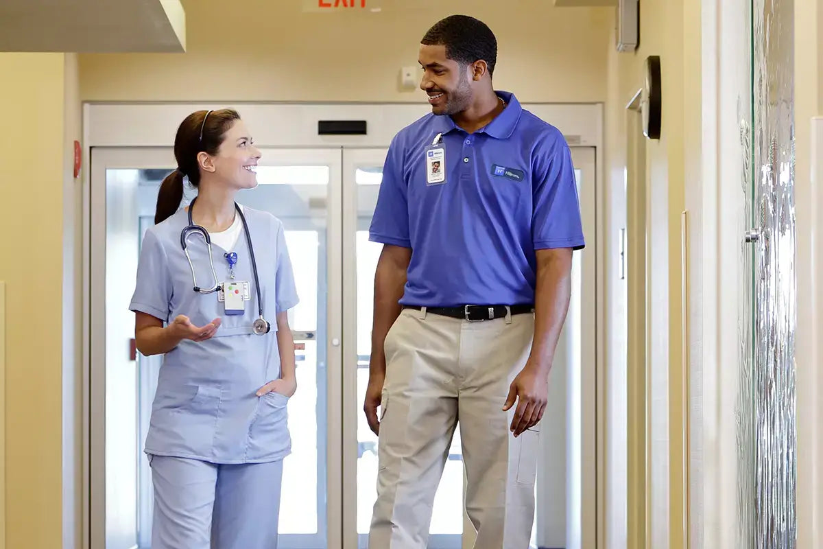 Two healthcare professionals, a nurse and a doctor, walking and talking in a hospital hallway.